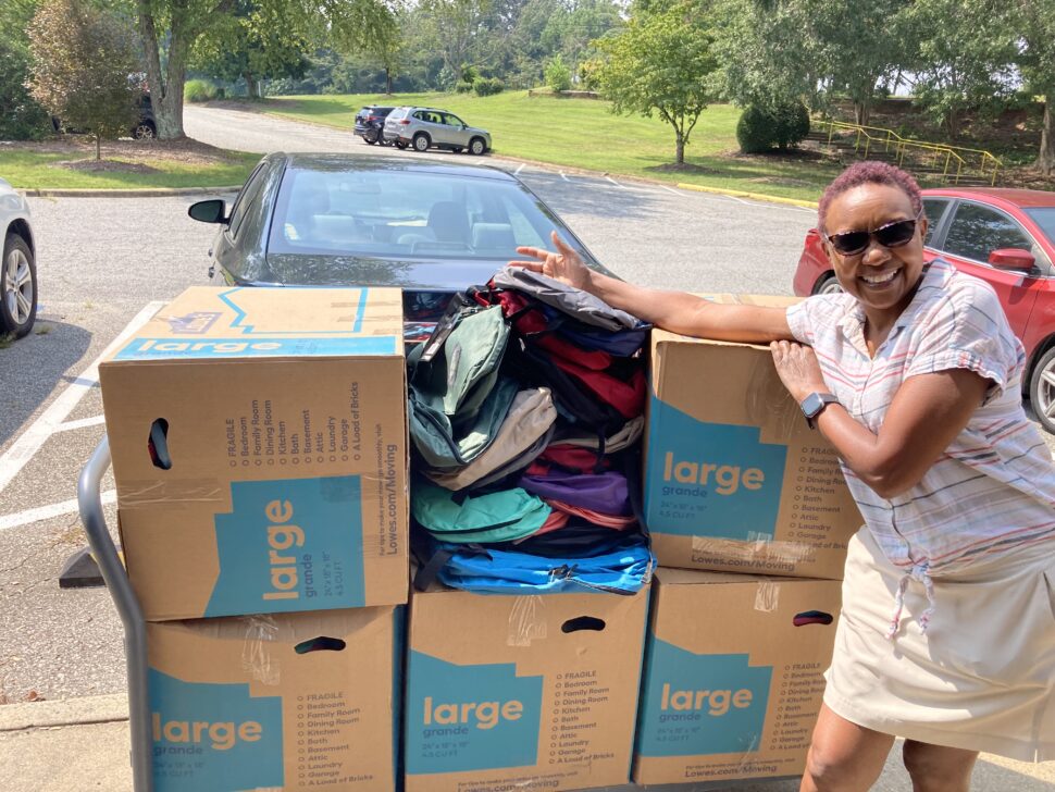 A photo of a woman standing with a lot of boxes packed with backpacks